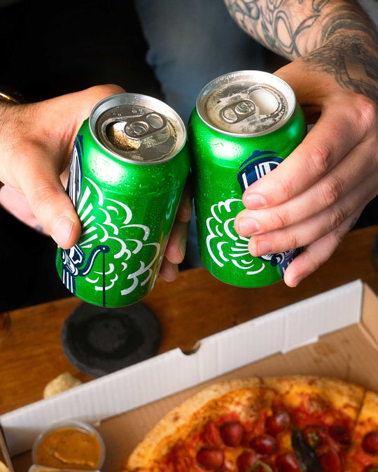 Two buds cheers-ing cans of Steam Whistle pilsner over a box of pep cup pizza